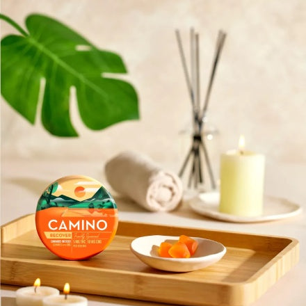Camino Freshly Squeezed Recover gummies with 5mg THC and 10mg CBG displayed on a wooden tray with candles.
