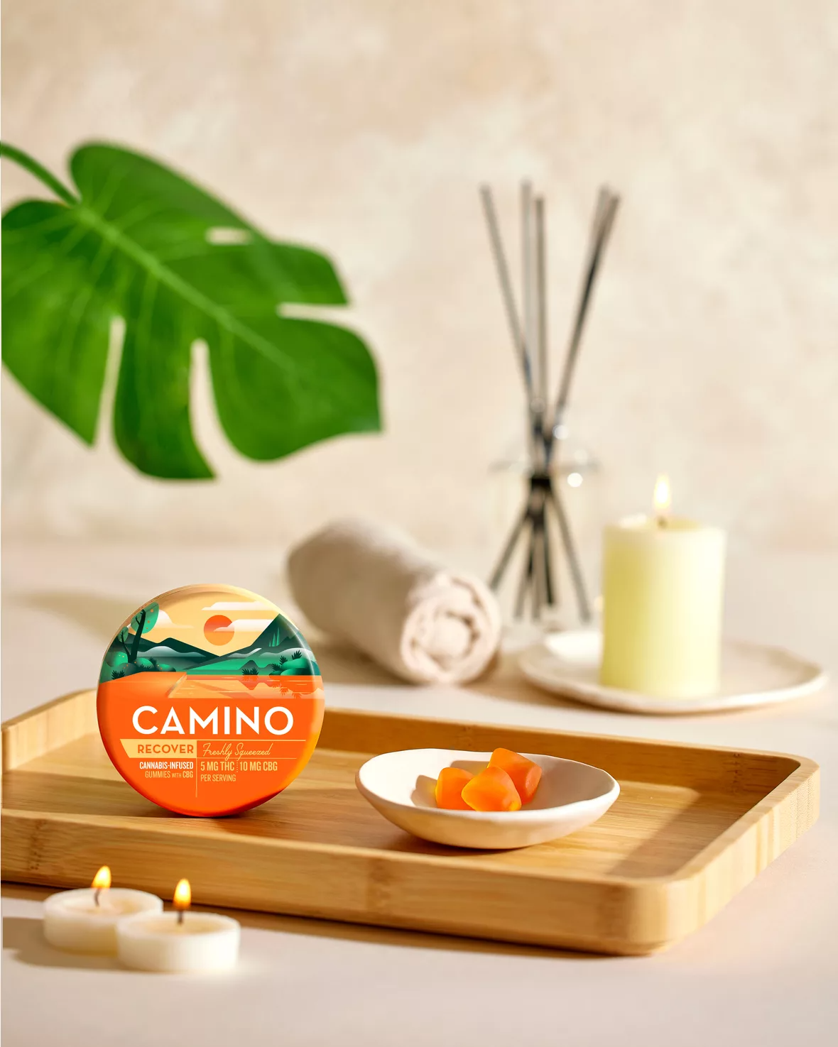 Camino Freshly Squeezed Recover gummies with 5mg THC and 10mg CBG displayed on a wooden tray with candles.