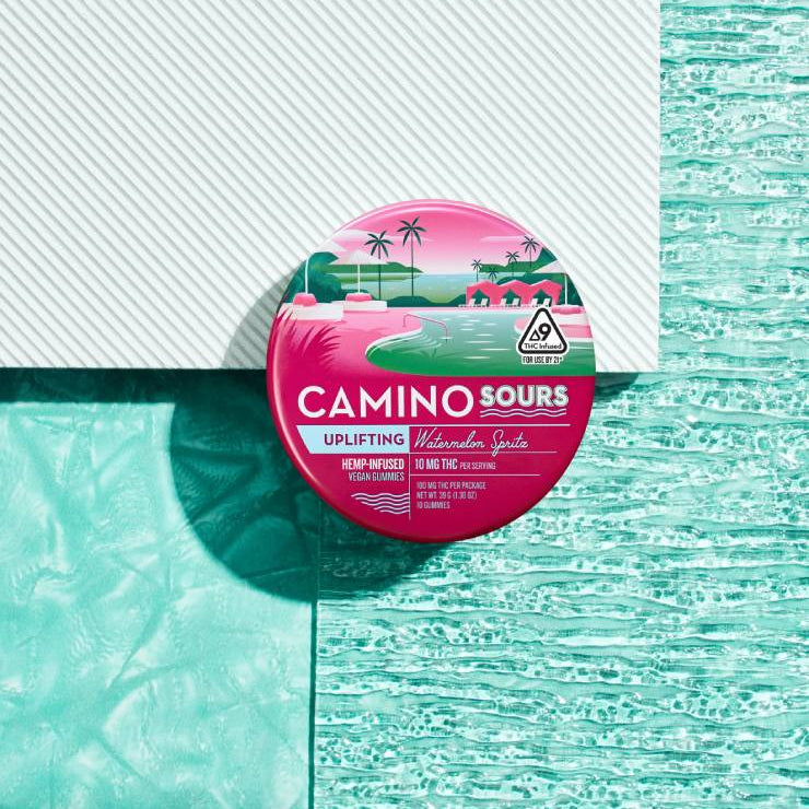 Pink and green watermelon spritz flavored hemp-infused gummies in a round container with tropical ocean and palm tree desi...