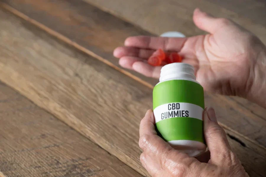 Older hands hold orange CBD gummies against a wooden background for a Wana fast asleep vs. Stay asleep gummies Goldfish Distro. article.